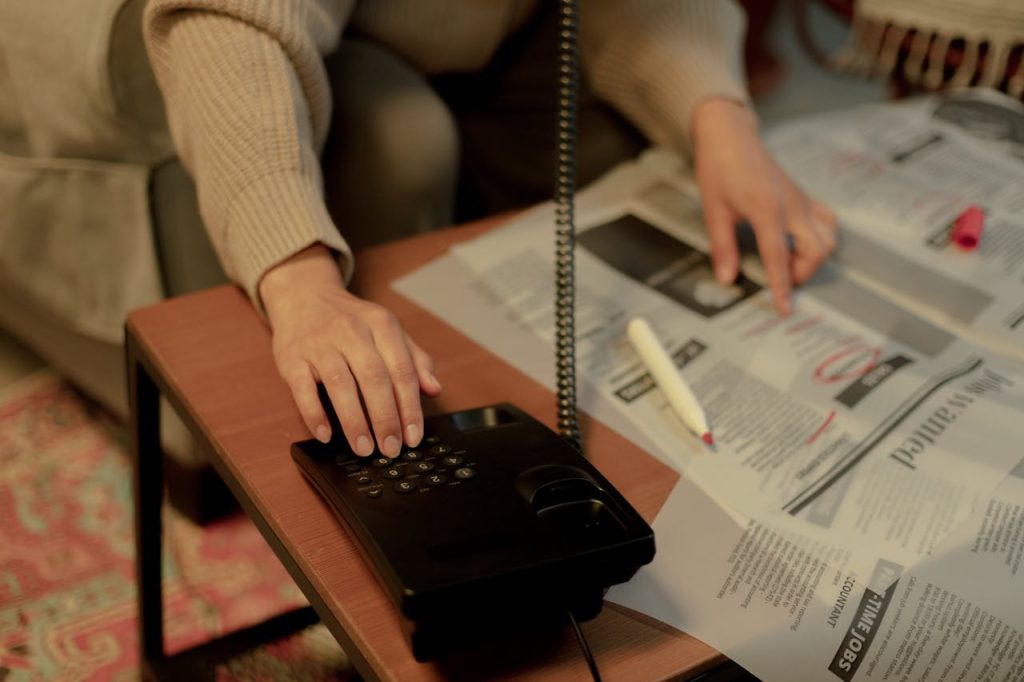 Woman using a landline and newspaper for a job search, highlighting domestic life.